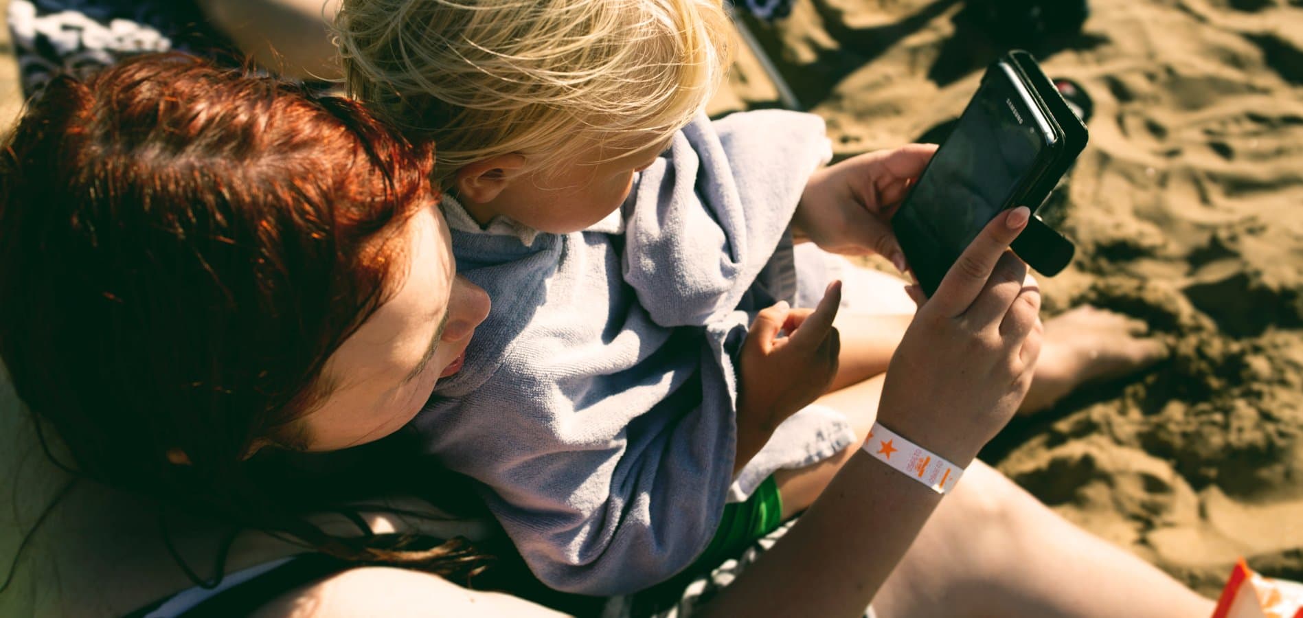 Mamma med barn tittar på telefon på stranden
