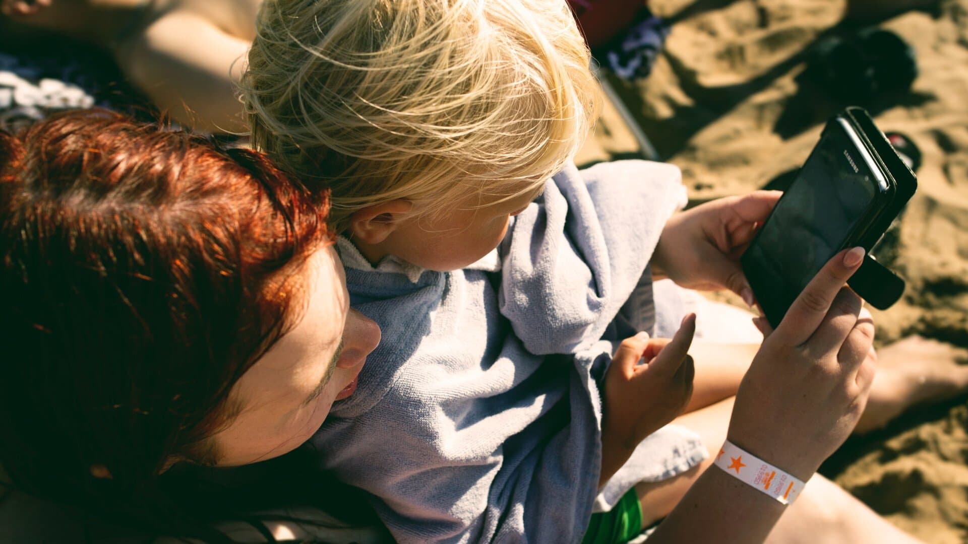 Mamma med barn tittar på telefon på stranden