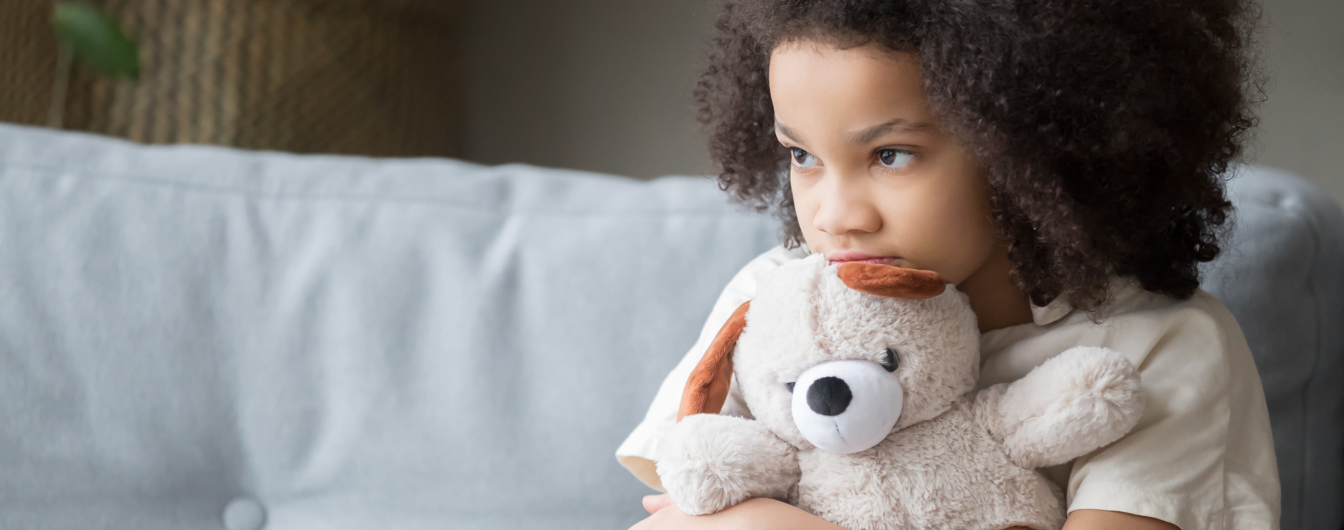 Barn med nalle Sorgset barn sitter i soffa med nalle i knÀt