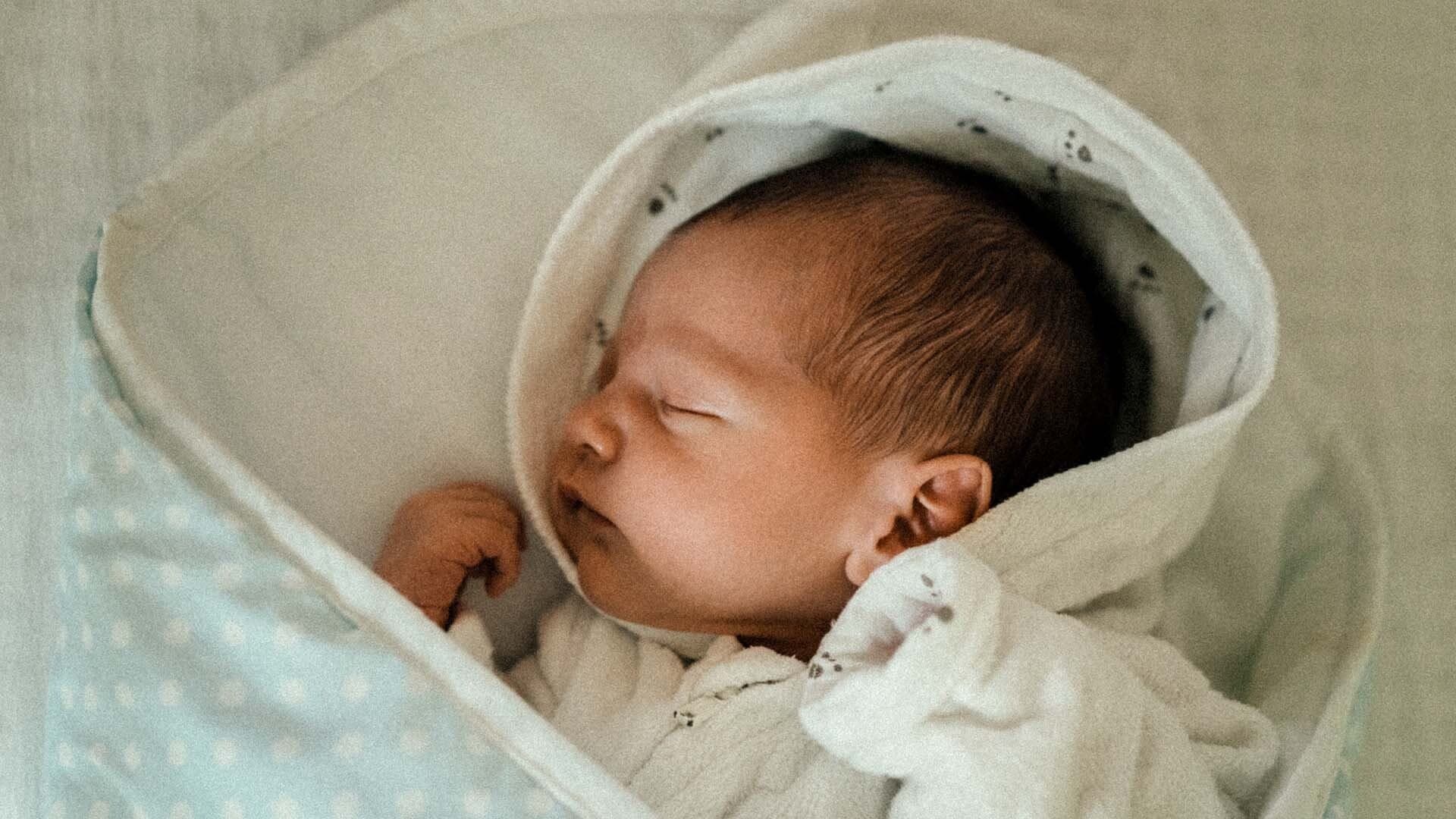 Sovande spÀdbarn Bebis sover nerbÀddad i ljusgrön filt med vita prickar