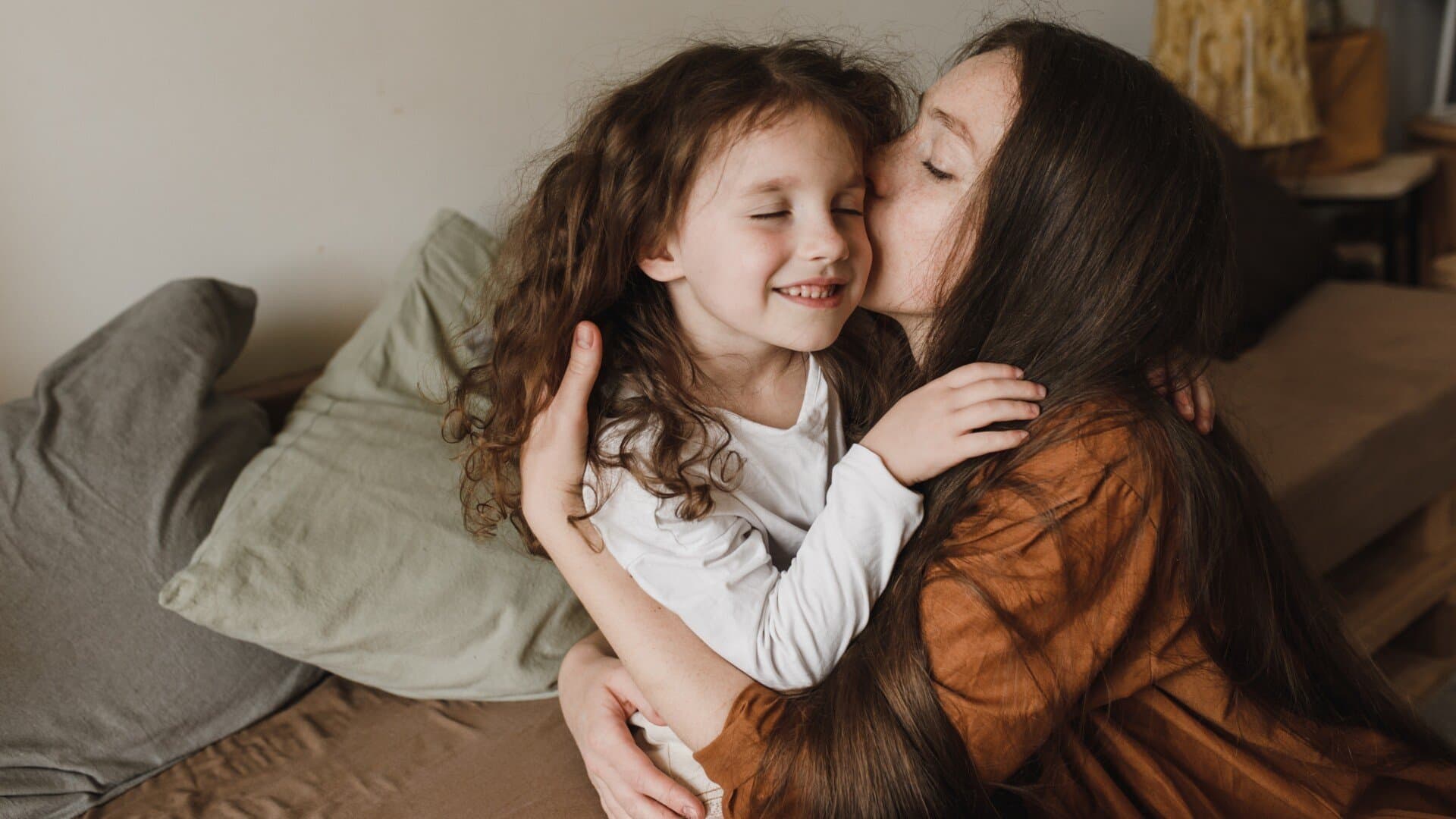 Mor och dotter Leende flicka med lockigt hÄr blir omfamnad och pussad av sin mamma