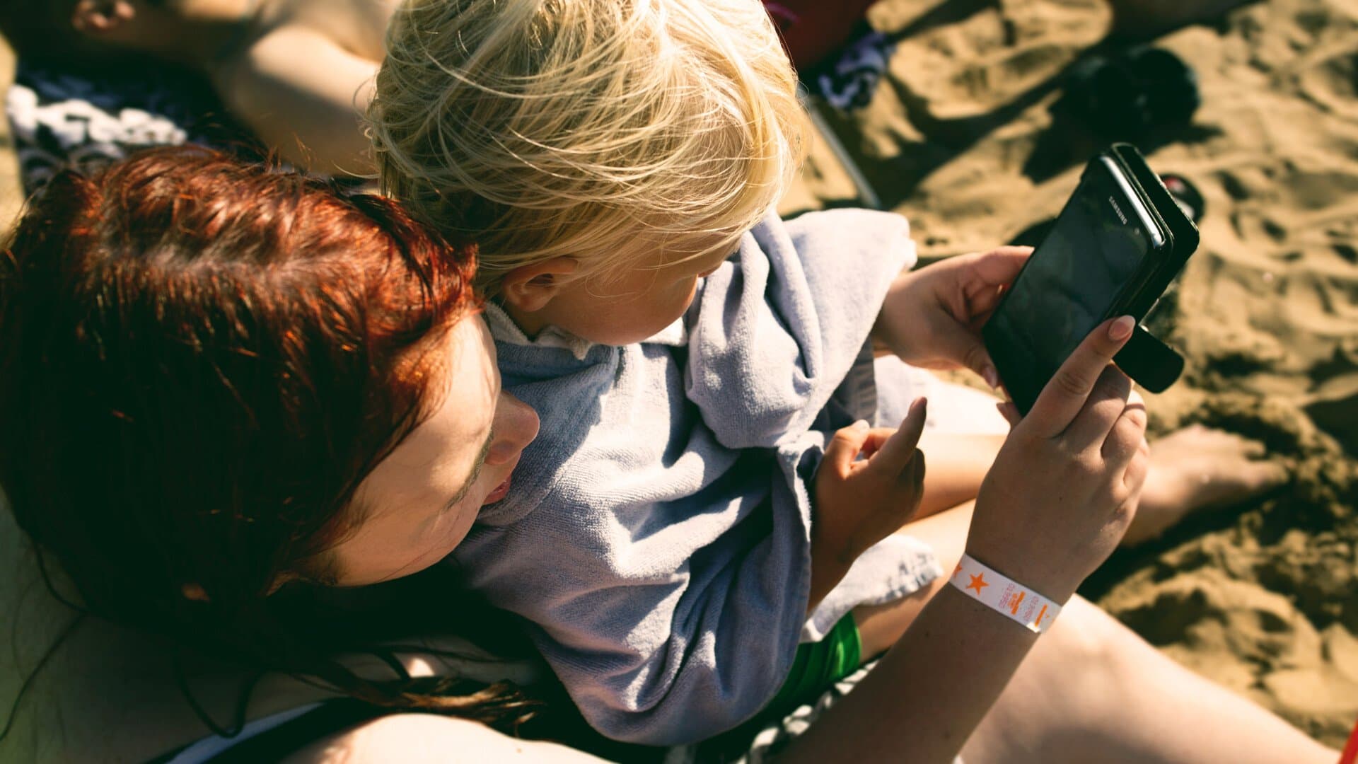 Mamma med barn tittar på telefon på stranden