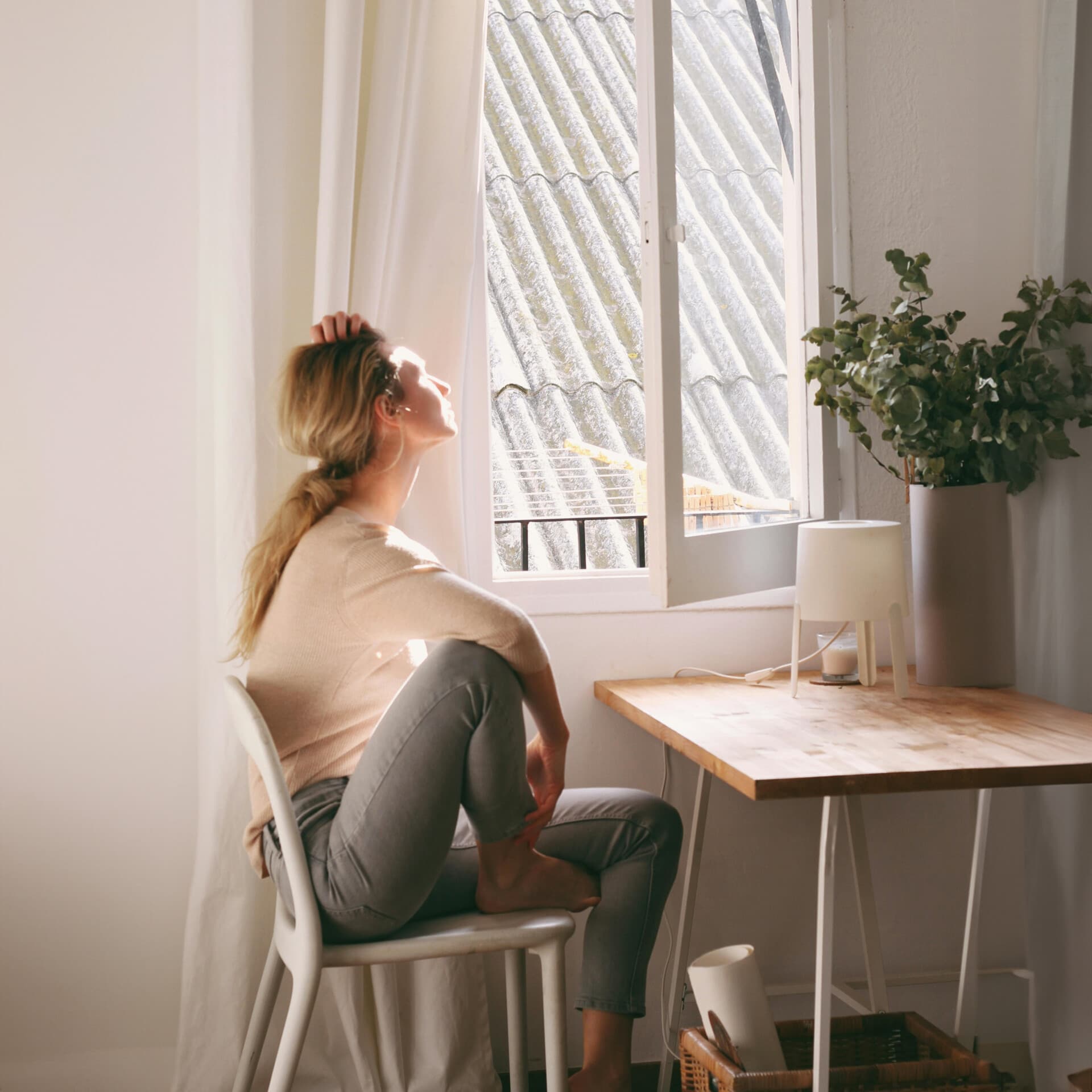 En kvinna sitter på en stol vid ett fönster En kvinna sitter på en stol vid ett fönster