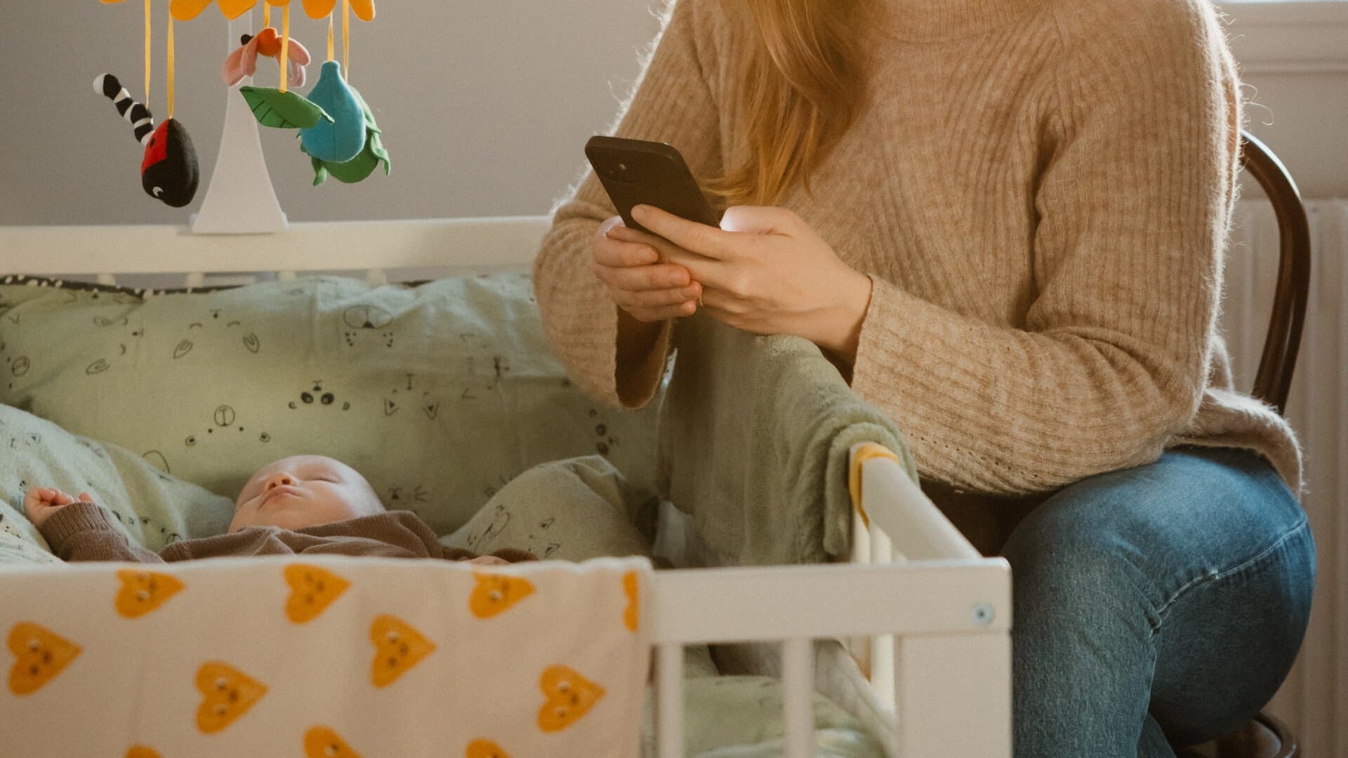 Mamma som sitter vid sin bebis och använder sin telefon